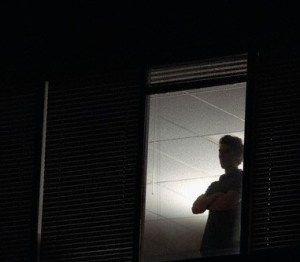 Man looking out office window at night